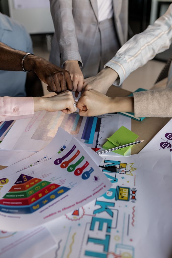 mission-img A group collaborates with a fist bump over colorful marketing charts, showcasing teamwork.